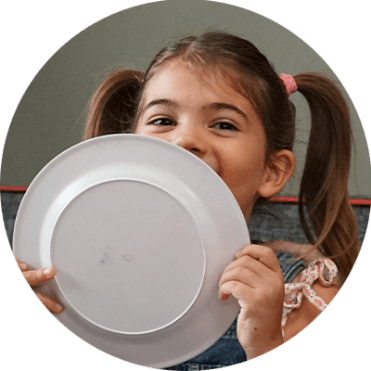 little girl holding a plate in front of her face